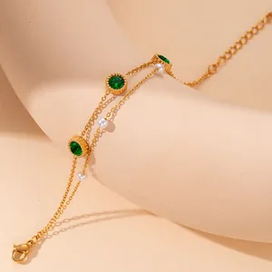 Double-layer gold chain bracelet with emerald green stones and pearls on beige prop