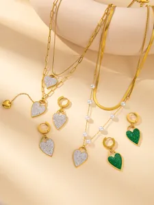 Close-up of gold-plated heart necklace with green crystal pavé and pearl chain detail