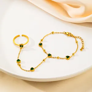 Dettaglio del bracciale ad anello dorato con pietre a cuore verdi su un piatto bianco