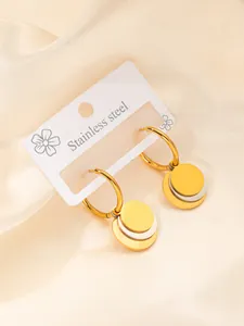 Détail de boucles d'oreilles en acier doré et argenté sur une élégante soie champagne