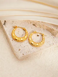 Detail of gold titanium hoop earrings with textured star patterns on beige stone and silk
