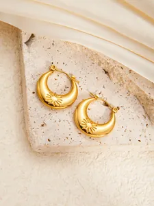 Macro shot of gold crescent earrings with sunburst texture on a stone surface