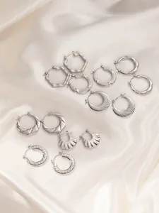 Macro shot of silver geometric earrings with various textured patterns on silk fabric