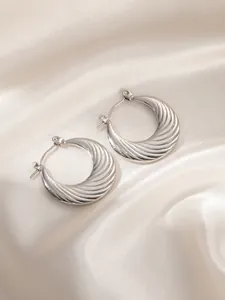 Detail of silver twisted hoop earrings with shell texture on white satin fabric