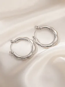 Close-up of silver-tone hoop earrings with irregular spiral texture on silk background