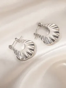 Detailed view of silver hoop earrings with fan-shaped shell texture on silk background