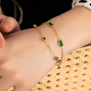 Detail of vintage gold layered bracelet with emerald cut green stone on model's wrist