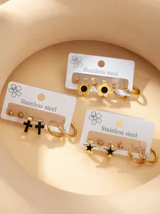 Makroaufnahme von Edelstahl-Ohrring-Set mit goldenen Kreuz- und Sternmotiven auf Karte
