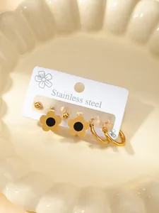 Detailliertes Set aus Edelstahl-Ohrringen mit Goldblumen und Kreuzdesigns auf Keramikschale
