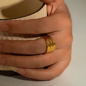 Gros plan d'une large bague en acier inoxydable doré avec motif matelassé au doigt