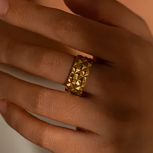 Vue détaillée d'une bague large en acier inoxydable doré avec texture pyramidale au doigt