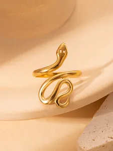 Detailansicht eines goldenen Edelstahlrings in Schlangenform auf einem Keramiksockel