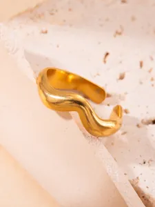 Detalle de un anillo ondulado dorado minimalista con acabado pulido sobre base de piedra
