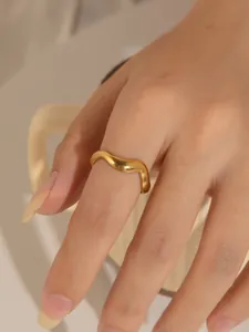 Primer plano de un anillo de acero de titanio dorado con diseño ondulado minimalista