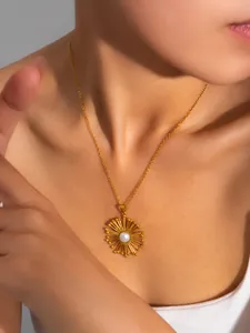 Detailed close-up of a golden sunburst pendant with pearl on a fine cross chain necklace