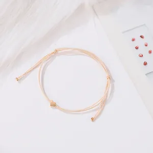 Bracelet cordon tressé crème minimaliste avec pendentif cœur doré sur fond blanc peluche