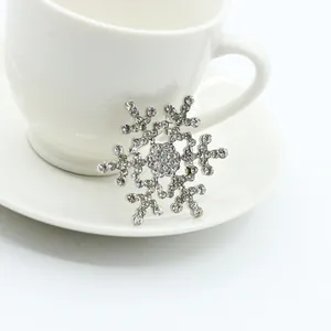 Silver snowflake brooch with sparkling rhinestones leaning on a white ceramic cup