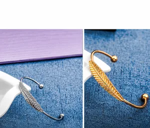 Dettaglio di bracciali a foglia regolabili in finitura oro e argento con trama a piuma