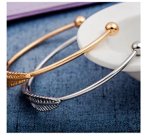 Dettaglio di bracciali a polsino con foglia di piuma in oro e argento su tessuto blu