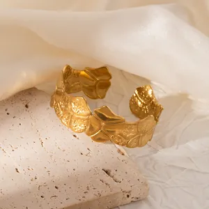 Macro detail of 18K gold-plated gingko leaf cuff with hammered texture on travertine
