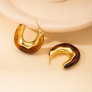 Dettaglio macro di orecchini a U dorati con resina ambrata su base in ceramica