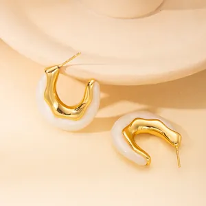 Dettaglio degli orecchini a perno a forma di U in metallo dorato e resina color crema