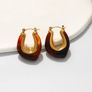 Detailed macro view of U-shaped gold-plated metal and amber resin earrings set on stone