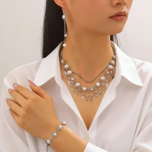 Dettaglio di collana di perle a strati e orecchini a croce indossati da una modella