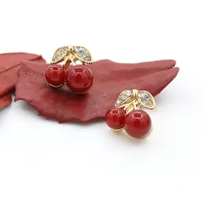 Detailed macro view of cherry stud earrings with red balls and crystal leaf detail