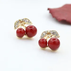 Close-up of gold cherry stud earrings with red beads and leaf-shaped crystal accents