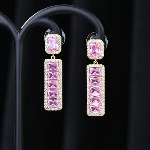 Dettaglio macro di orecchini dorati con zircone rosa rettangolare e pietre bianche
