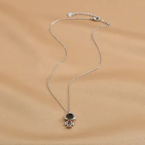 Détail du collier astronaute argenté avec un petit cœur rouge sur tissu en satin