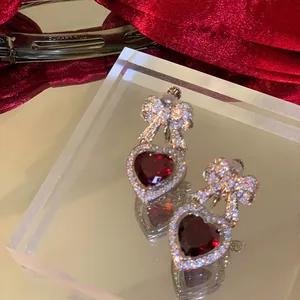 Dettaglio di orecchini a cuore rosso con fiocco di diamanti in stile festivo