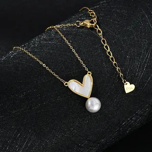 Dettaglio di una collana dorata con pendente in madreperla a cuore e perla bianca tonda