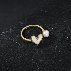 Dettaglio anello dorato con perla bianca e intarsio a cuore su sfondo nero scuro