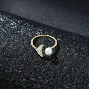 Detail of gold open ring featuring a white mermaid tail shell and round pearl accent