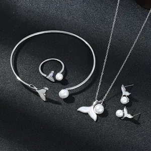 Detailed view of silver mermaid tail jewelry set with pearls on grey textured surface