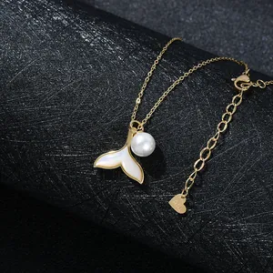 Detailed close-up of a gold fishtail pendant with white shell inlay and a round pearl