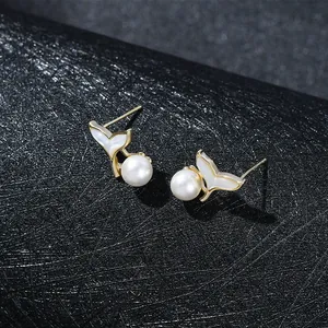 Macro shot of elegant gold fishtail earrings with glossy white pearls on black texture