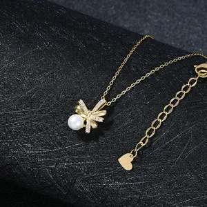 Dettaglio della collana a fiocco dorato con micro diamanti e perla bianca tonda