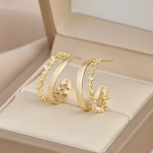 Elegante C-förmige zweischichtige Goldohrringe mit Zirkonia-Steinen in einer Schmuckschatulle