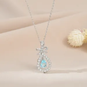 Collier nœud argenté avec pendentif goutte d'eau bleu clair sur tissu couleur champagne