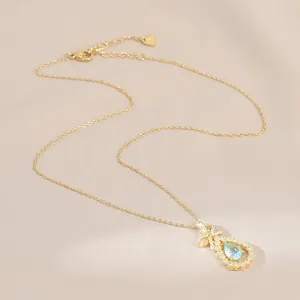 Détail du collier doré avec pierre bleue en goutte, nœud en diamant et pendentif cœur