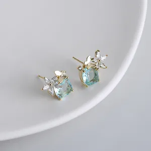 Dettaglio di orecchini blu a cuscino con farfalla dorata e accenti floreali in zircone