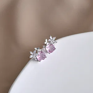 Vista macro di orecchini con pietra rosa quadrata e dettagli a farfalla d'argento