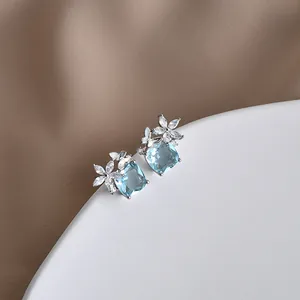 Dettaglio orecchini a farfalla con gemma blu quadrata e petali di fiori in zircone