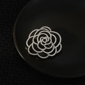 Macro detail of silver camellia brooch with hollowed petals and sparkling zircons