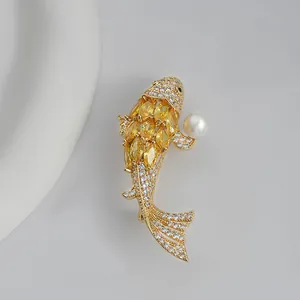 Golden koi fish brooch with yellow rhinestones and a white pearl on a minimal grey backdrop