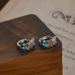 Dettaglio di orecchini a C con zirconi arcobaleno su legno in stile vintage