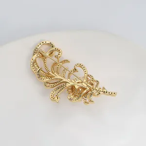 Détail macro d'une broche plume dorée avec fermoir de sécurité et pavé de cristaux